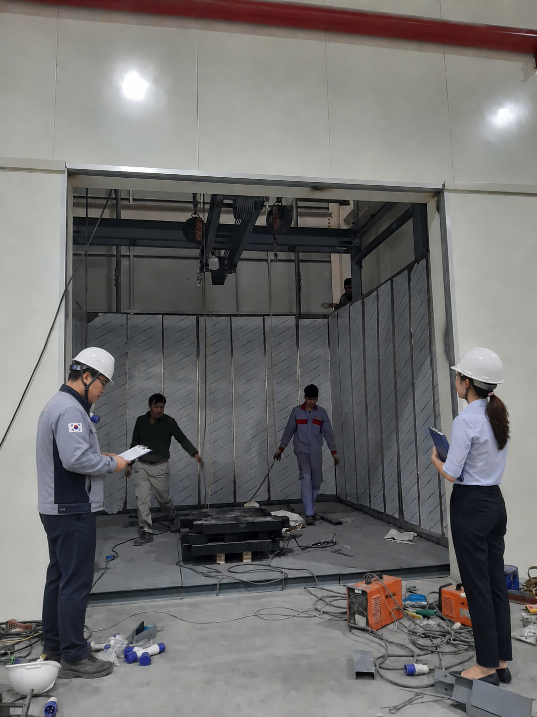Kỹ sư giám sát lắp đặt thiết bị công nghiệp trong phòng máy với công nhân thi công bên trong